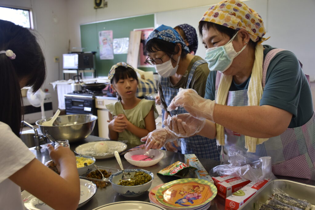 学童の子供たちにおにぎりの作り方を教える石川美知子部長（右）